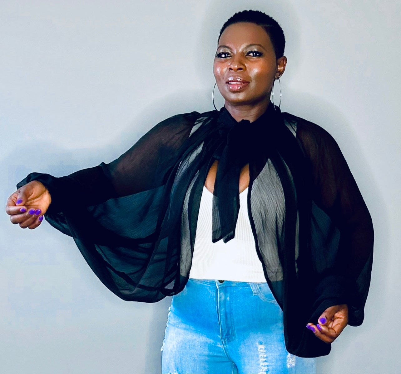 Model wearing a black organza blouse with sheer balloon sleeves and structured cuffs.