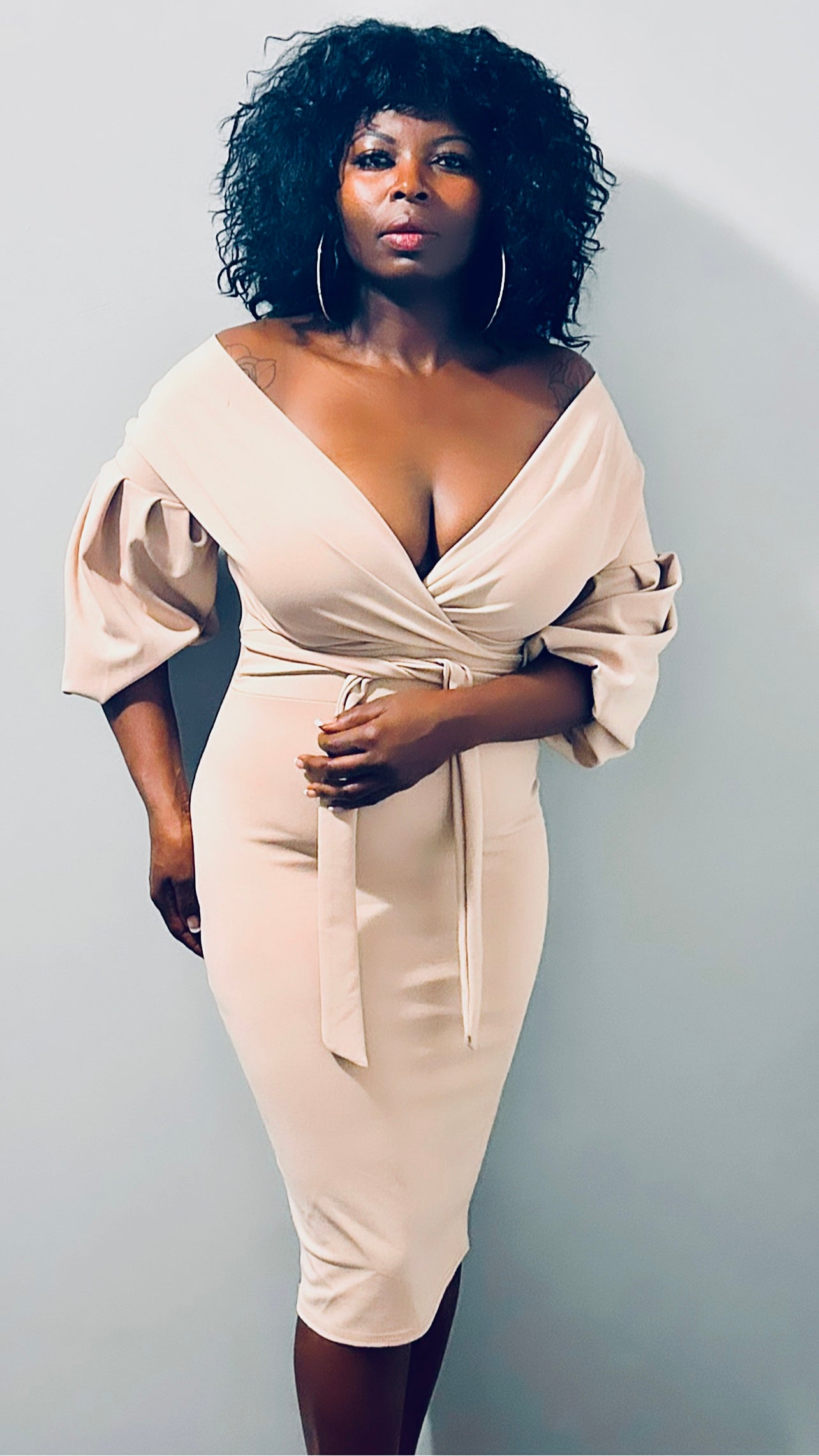 Model wearing a nude belted bodycon midi dress with off-the-shoulder sleeves.