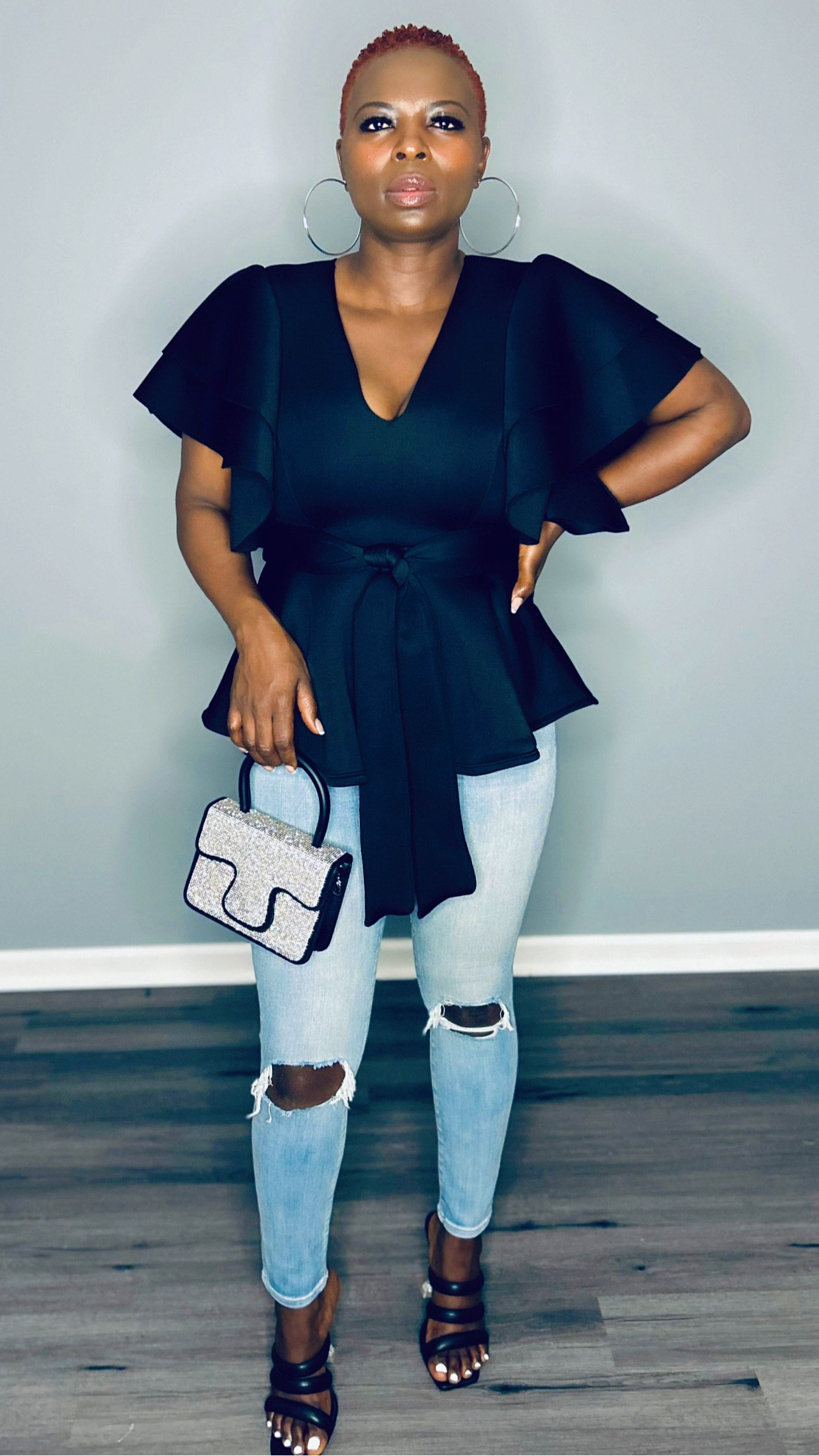 lack deep v-neck top with ruffle sleeves, matched with a handbag and high heels.